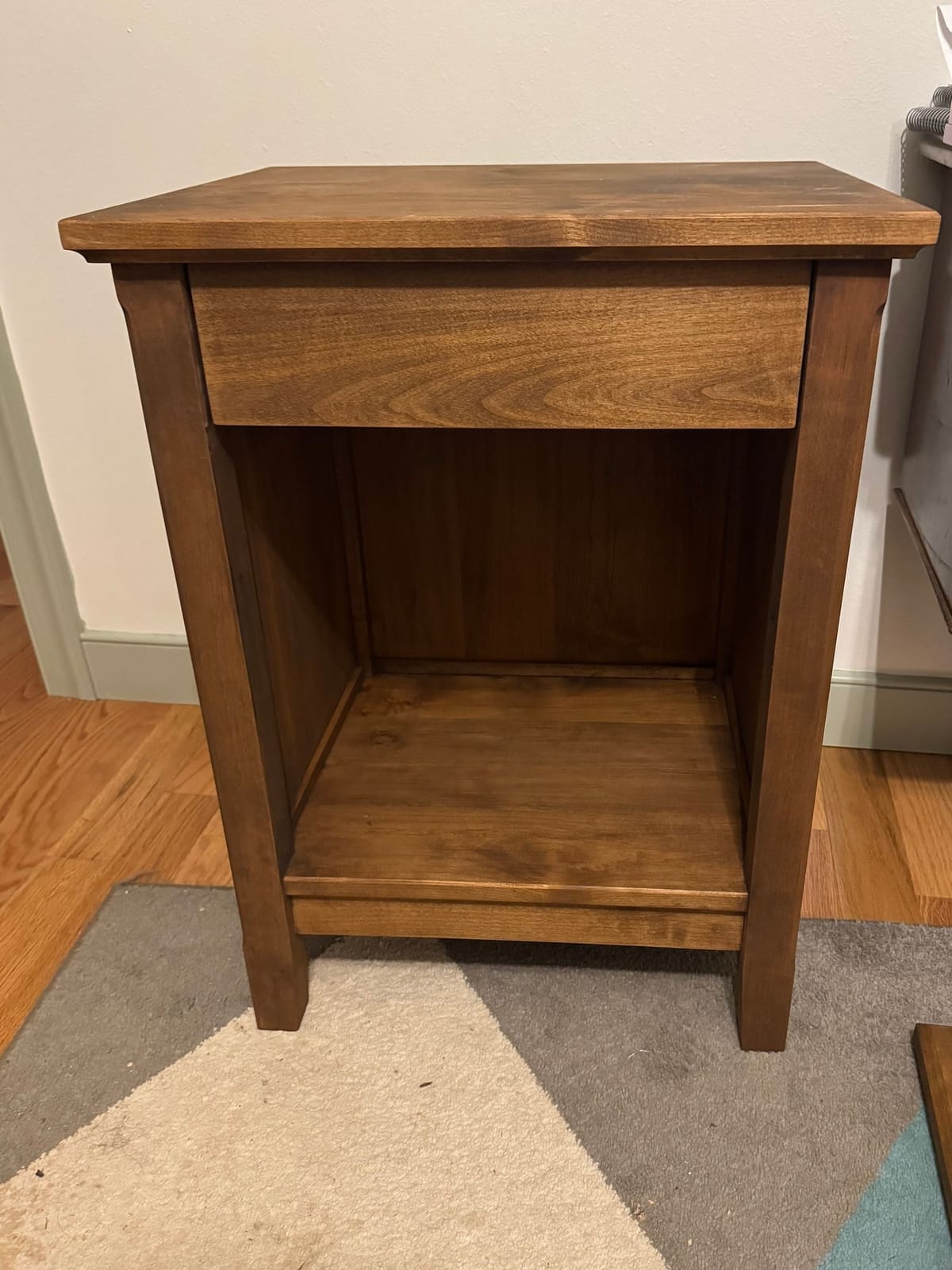 Stained nightstand in a bedroom, with one drawer and an open lower shelf