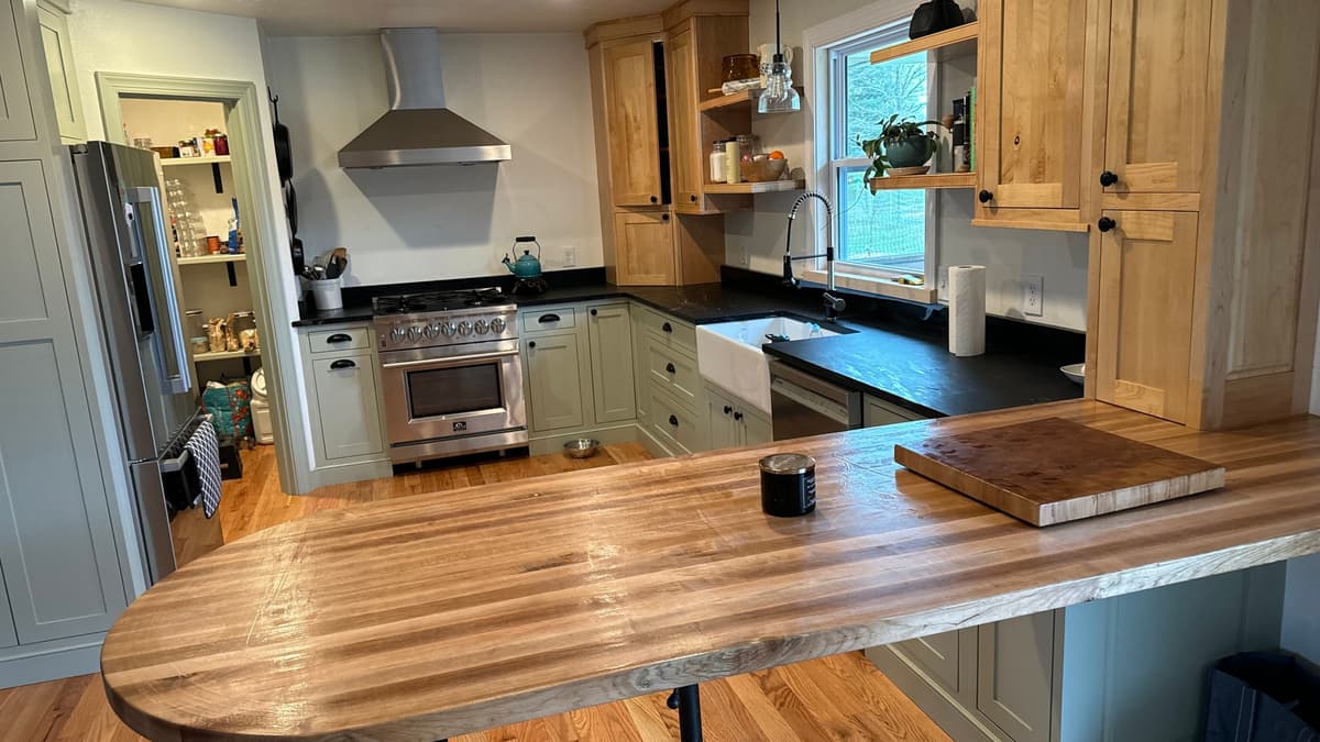 Kitchen with sage green lower cabinets, natural wood uppers and a butcher-block peninsula