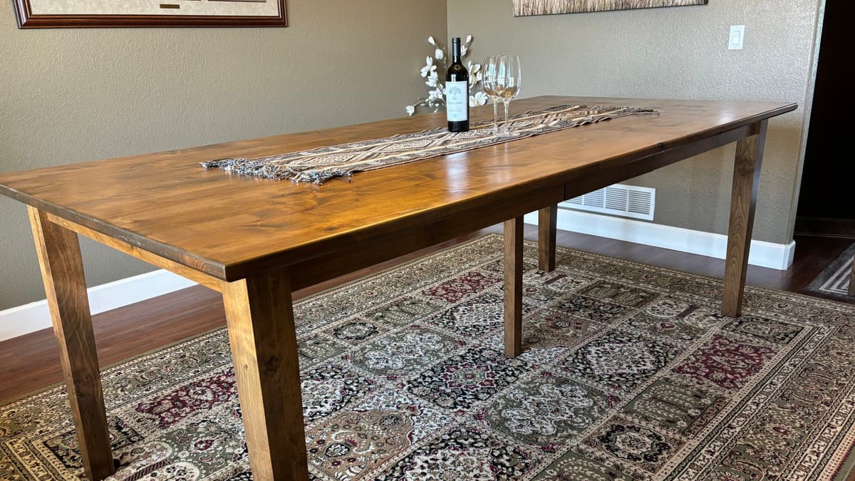 Dining table with tapered legs and a warm brown stained top on a patterned rug