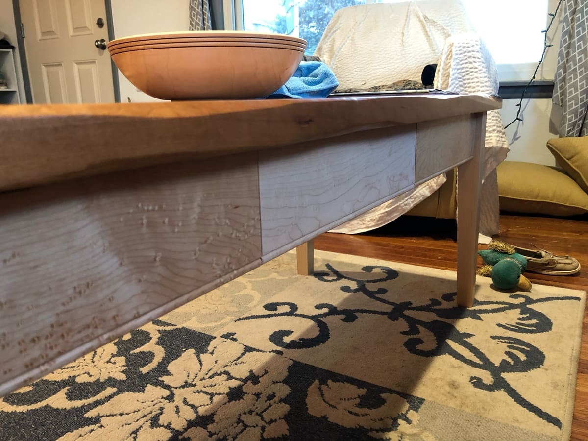 Low view of a table apron in bird's-eye maple under a natural edge top, with pale legs