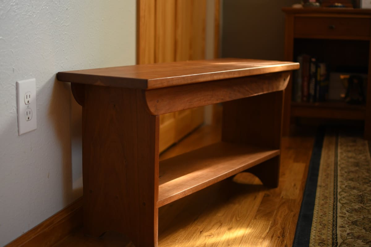Wood bench with a curved apron, arched cutout feet and a lower shelf in warm low sunlight