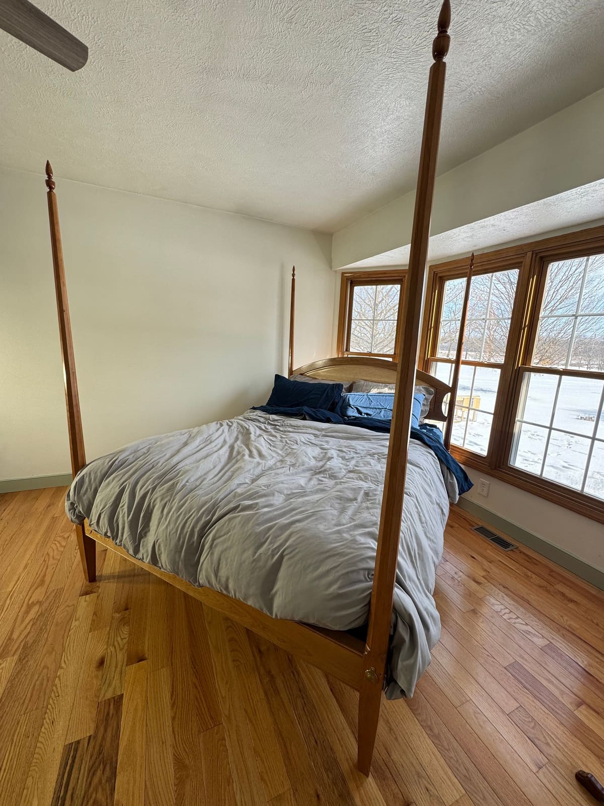 Four-poster bed with tall tapered posts and finials and an arched headboard in a sunlit bedroom