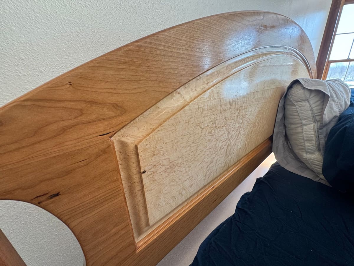 Arched headboard with a raised bird's-eye maple panel set in a solid wood frame, seen at an angle