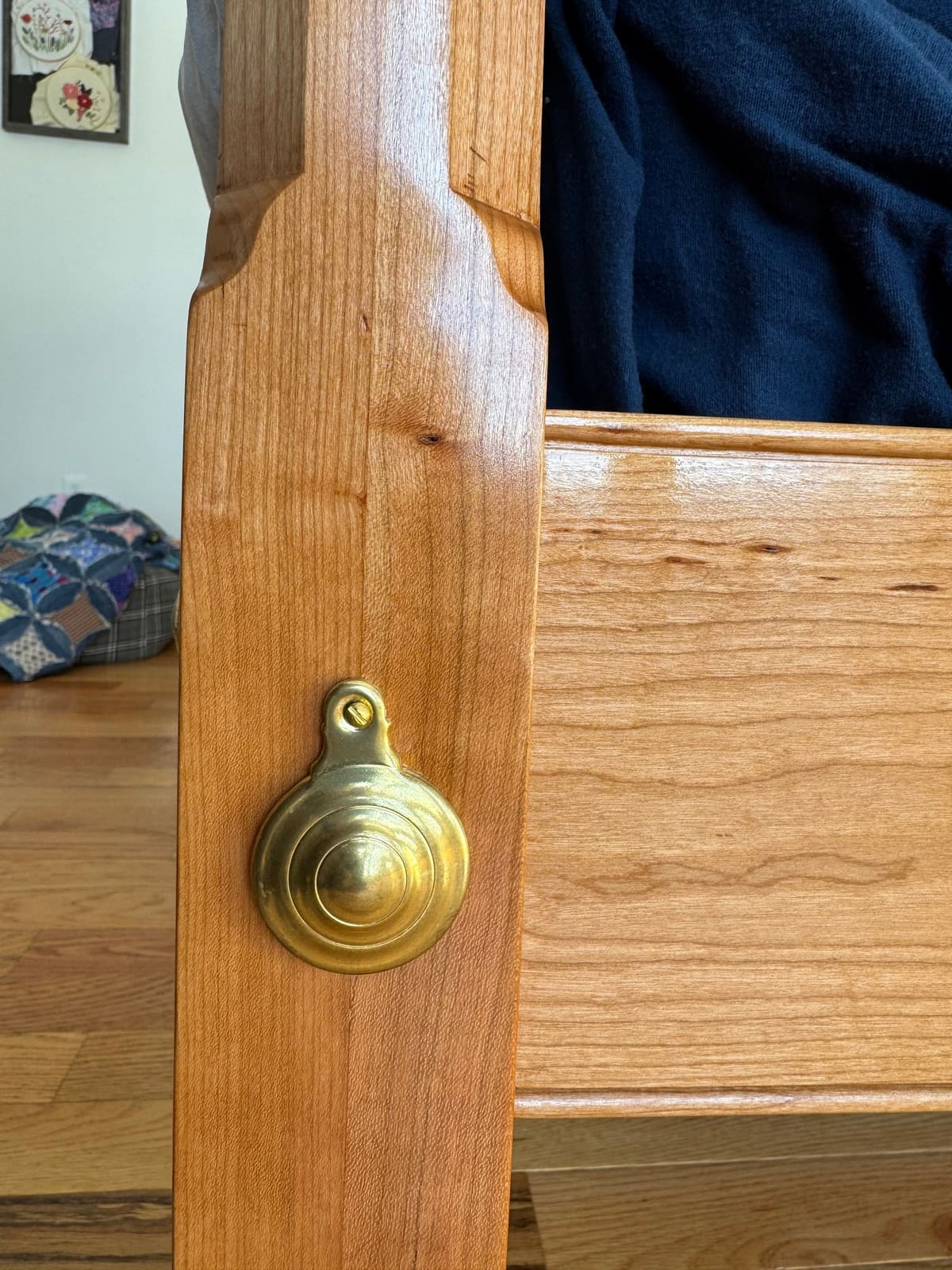 Close-up of a bed post with a round brass bolt cover and a stopped chamfer above the rail