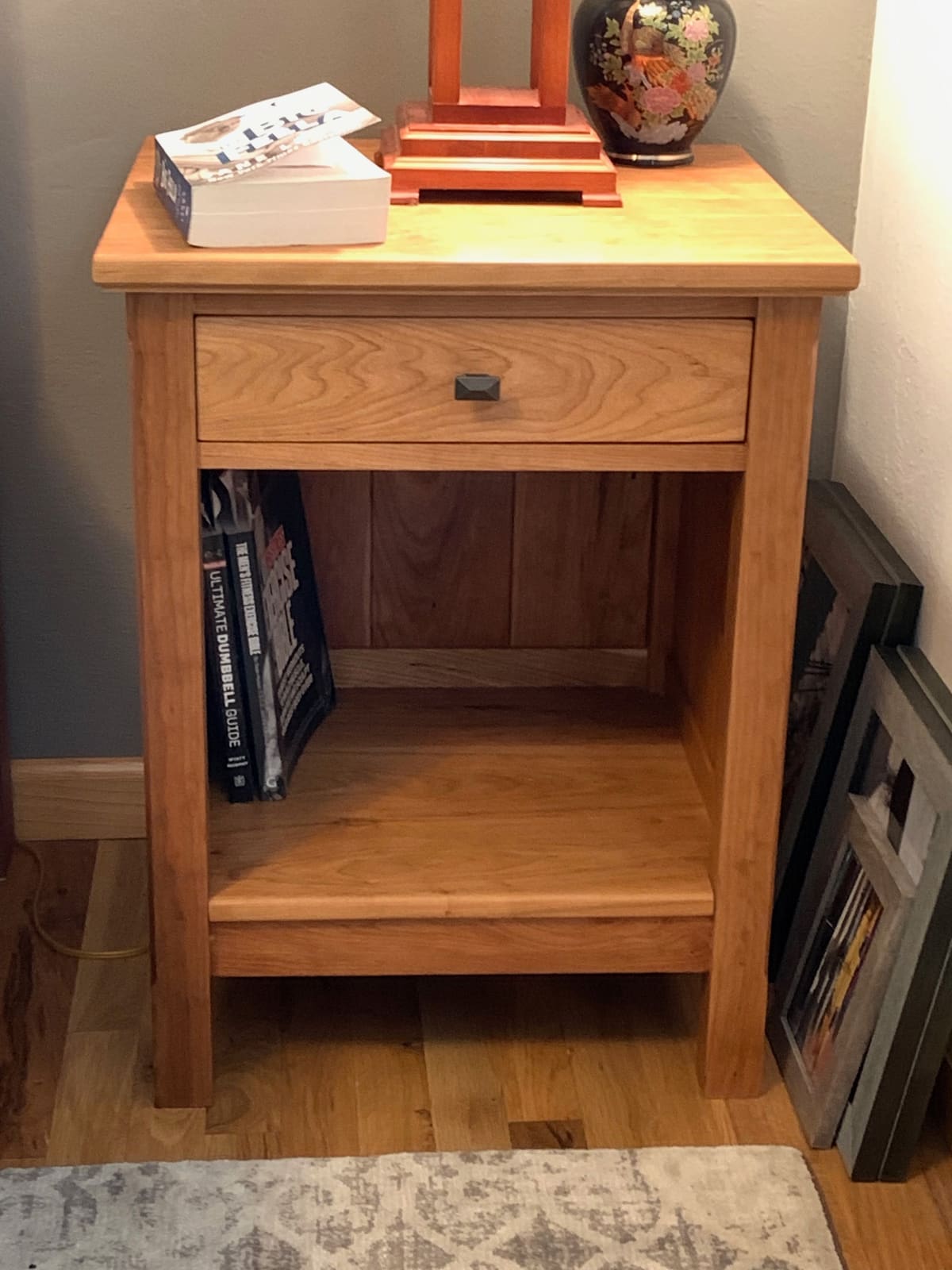 Nightstand with one drawer, a dark metal knob, an open lower shelf and a plank back panel