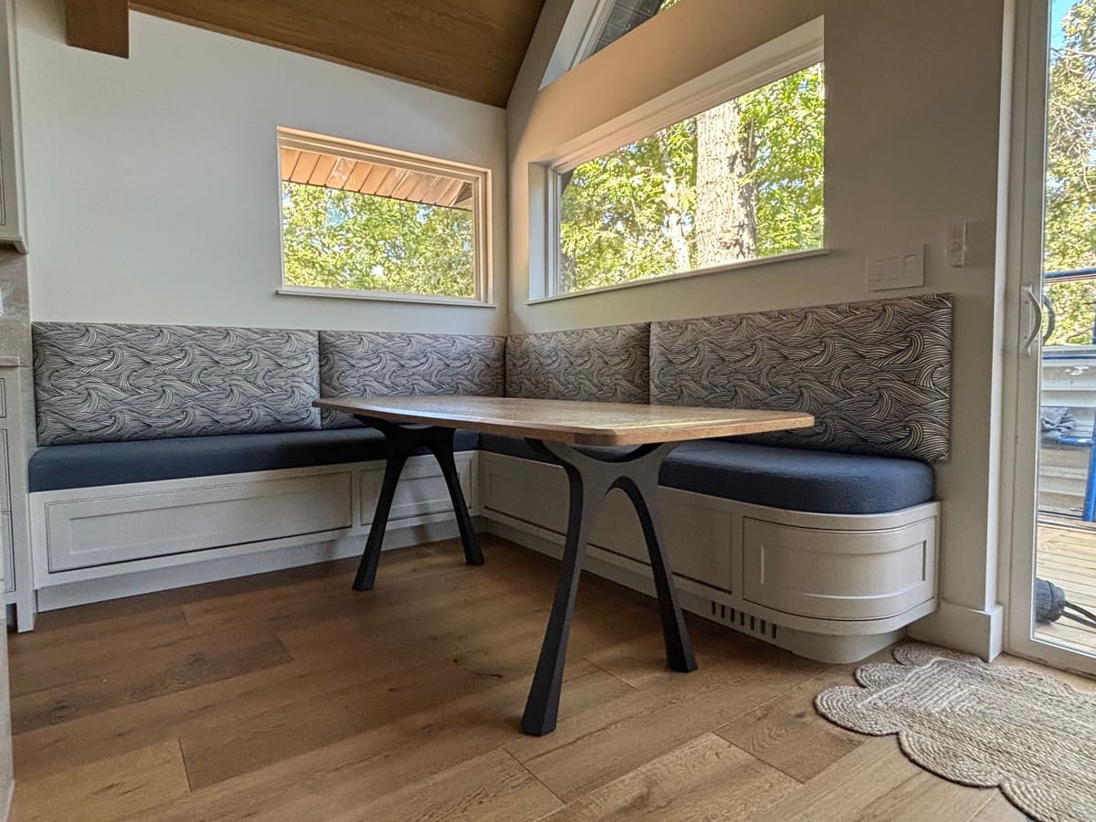 L-shaped built-in banquette with painted panel bases, a curved end cabinet, and a wood table on black steel legs