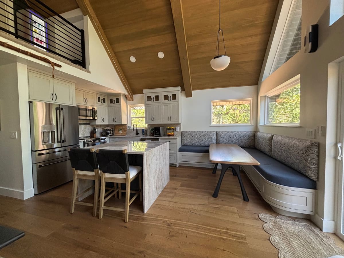 Curved built-in banquette and wood table at the end of an open kitchen under a vaulted wood ceiling