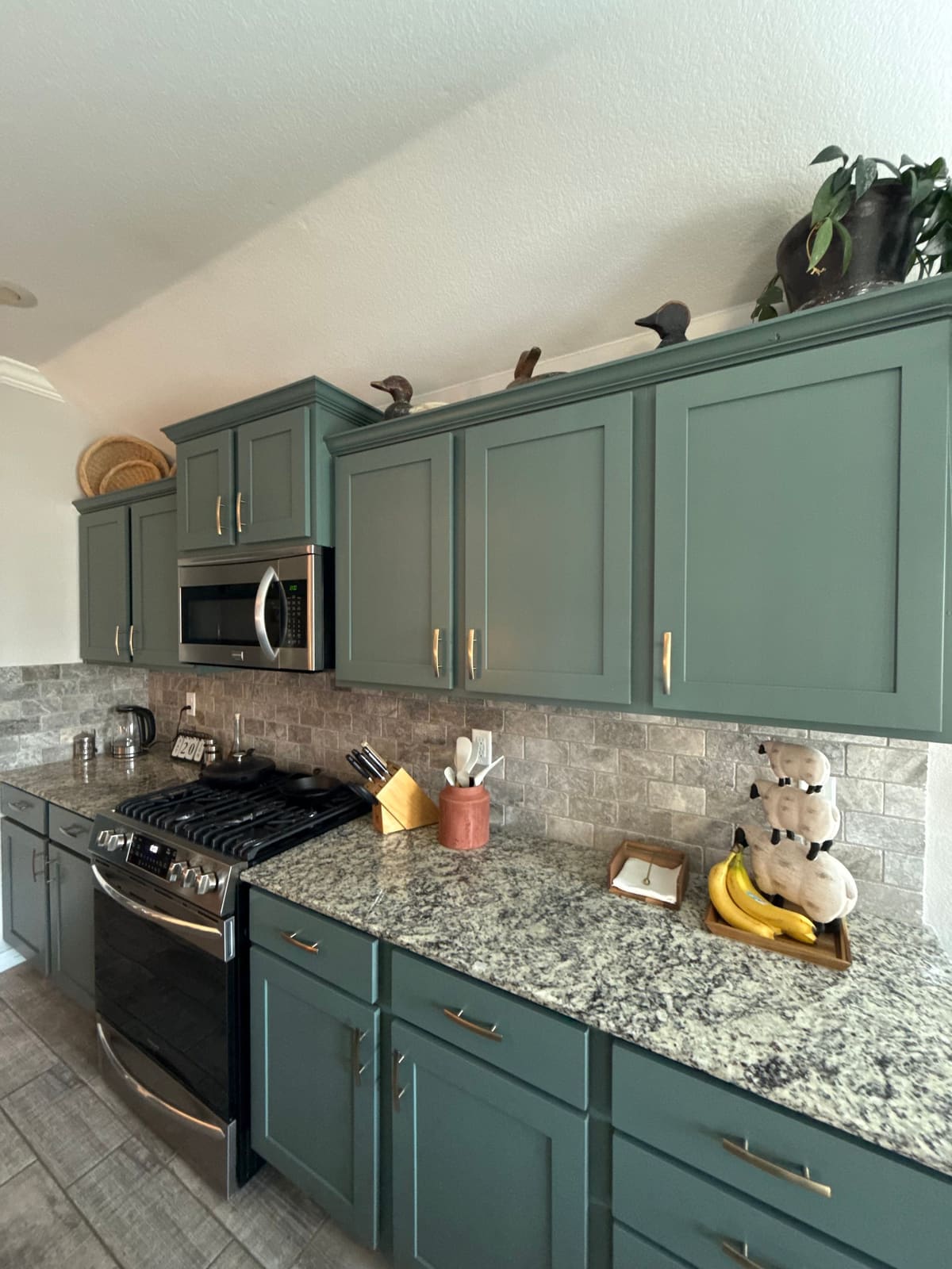 Kitchen wall of deep green shaker doors and drawer fronts with brushed brass pulls and staggered upper cabinets