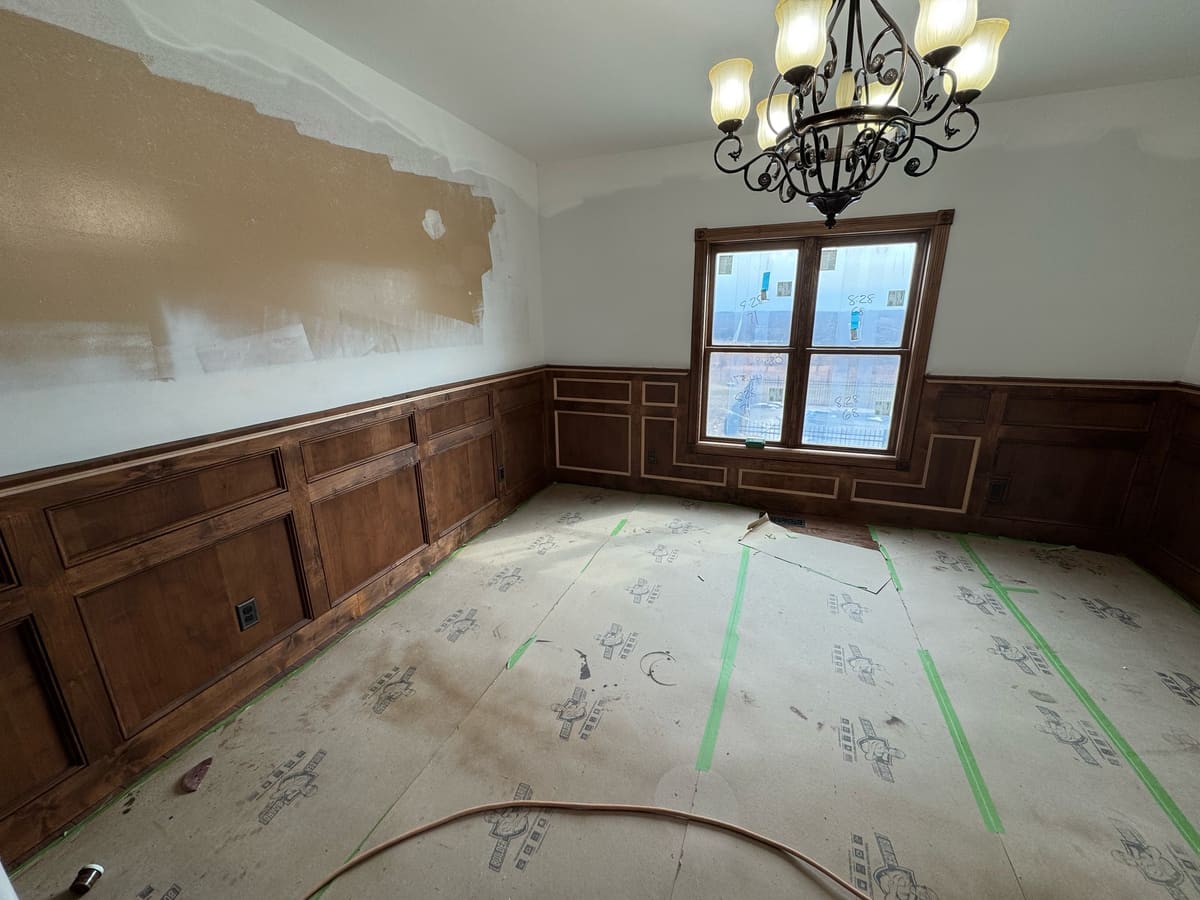 Dining room with stained wood panel wainscoting and chair rail around the walls and window, during construction