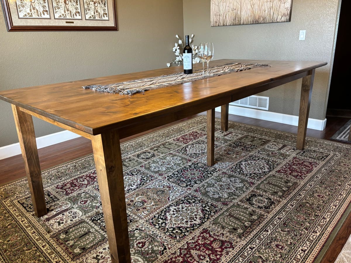 Rectangular dining table with tapered legs and a warm brown stained top on a patterned area rug