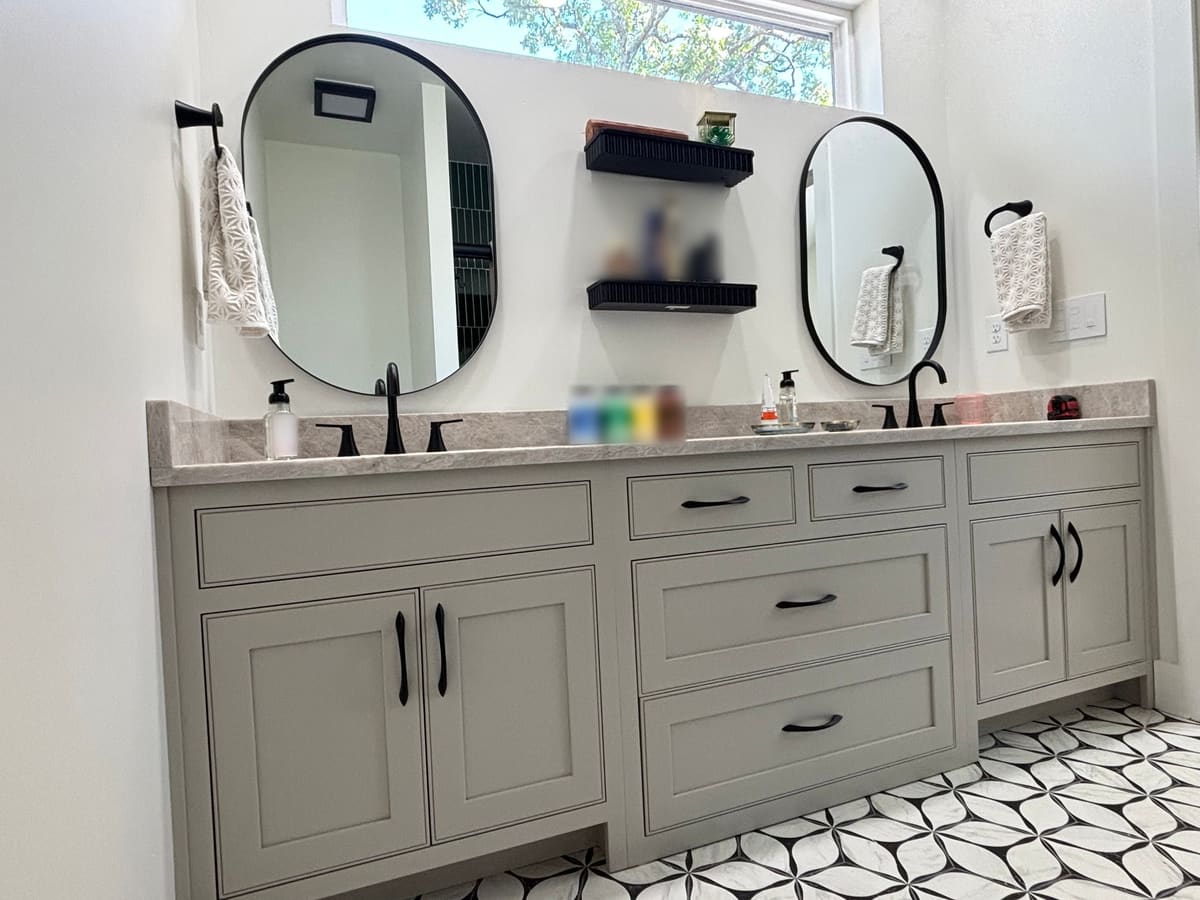 Light gray double vanity with inset shaker doors and drawers, black pulls, and a stone countertop