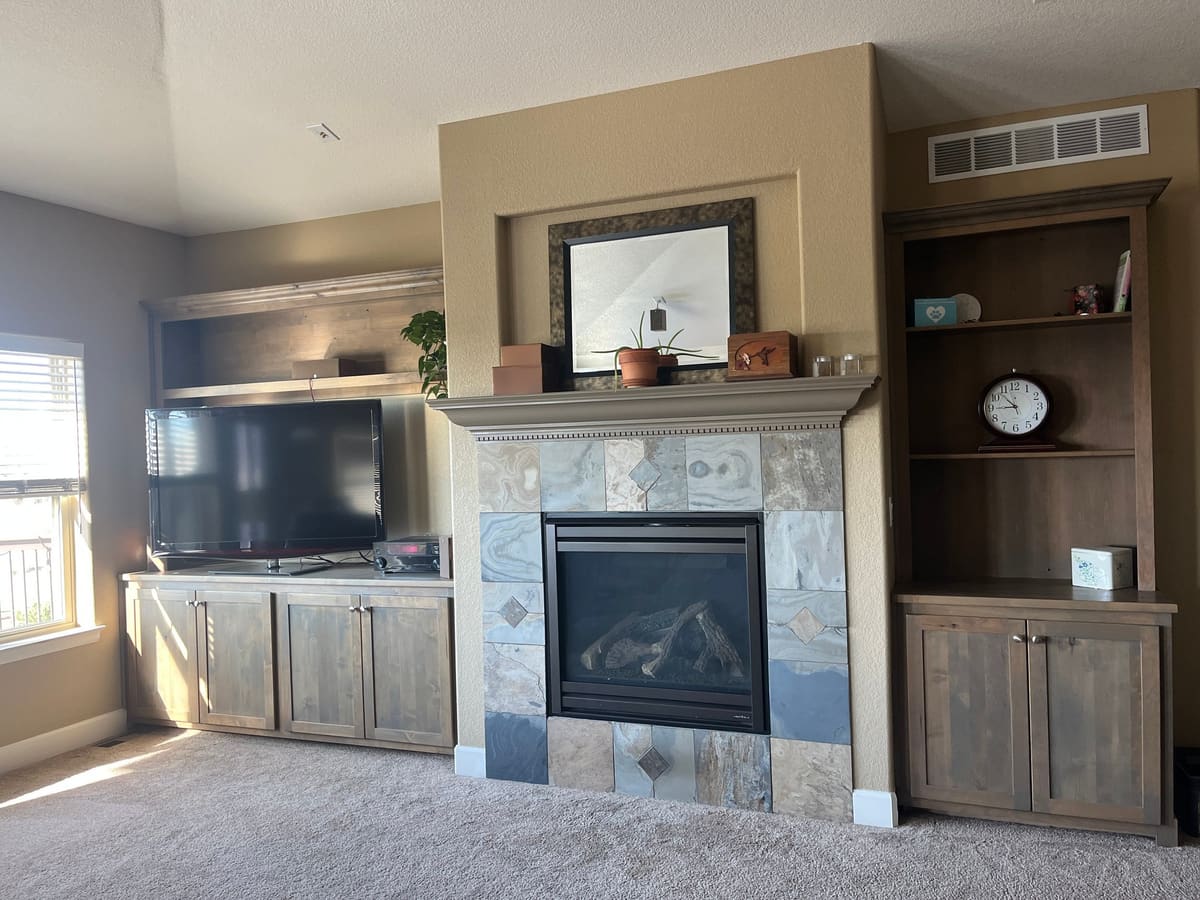 Angled view of stained built-in media cabinet and bookcase on either side of a slate tile fireplace