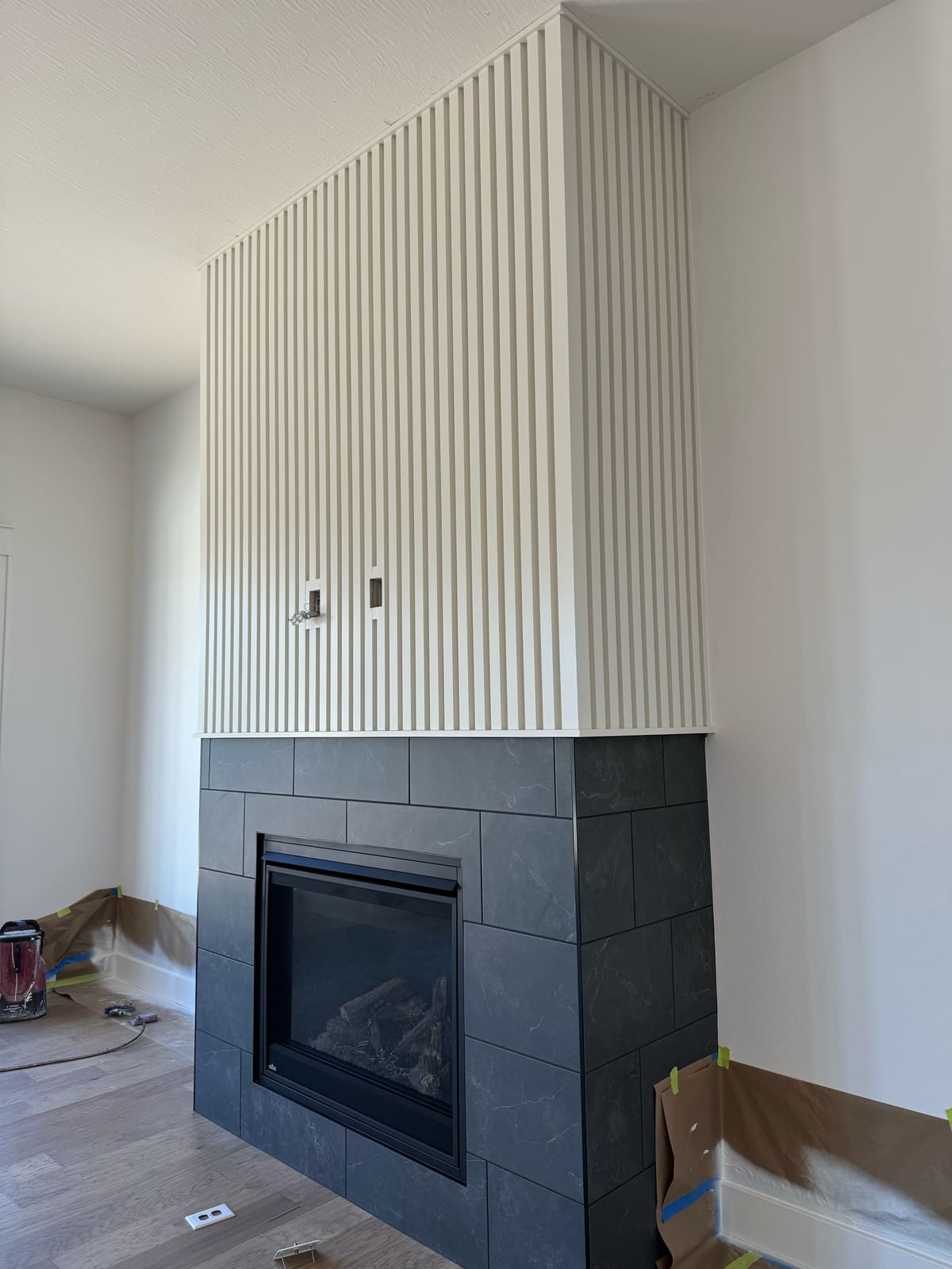 Fireplace with a floor-to-ceiling painted vertical slat overmantel above a charcoal tile surround