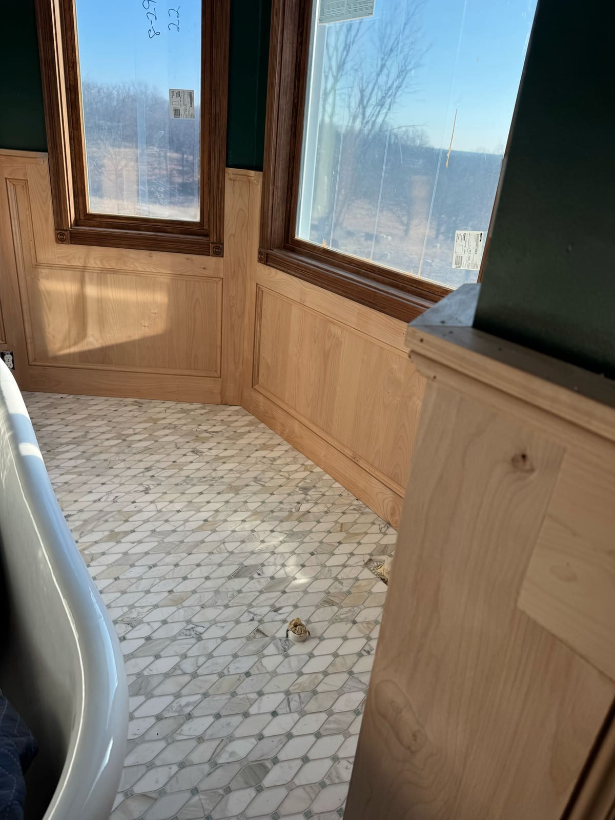 Unfinished raised-panel wainscot around a bay window with dark stained casings in a bathroom under construction