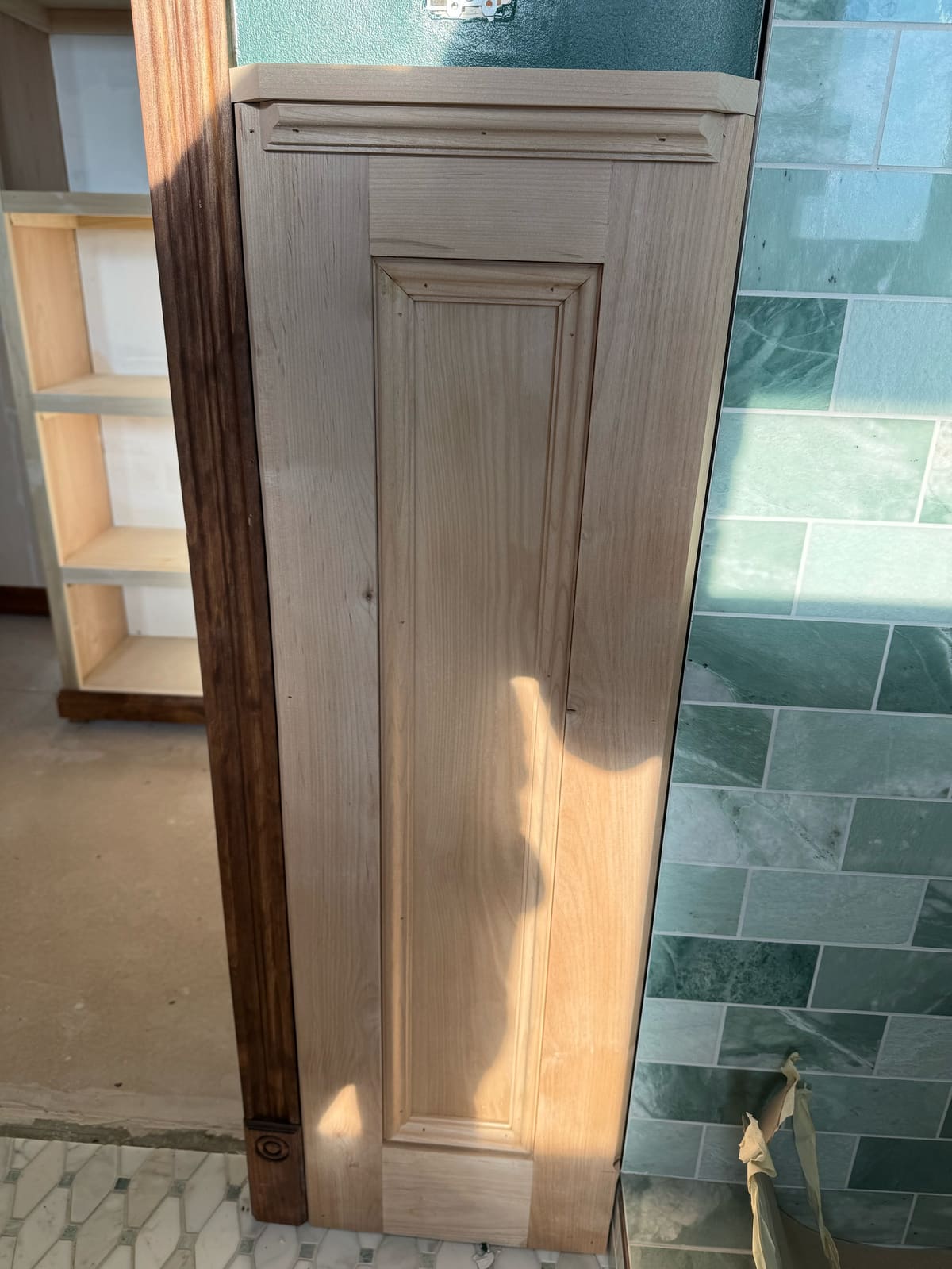 Unfinished raised wood panel with cap molding beside a green tile shower wall during a bathroom build