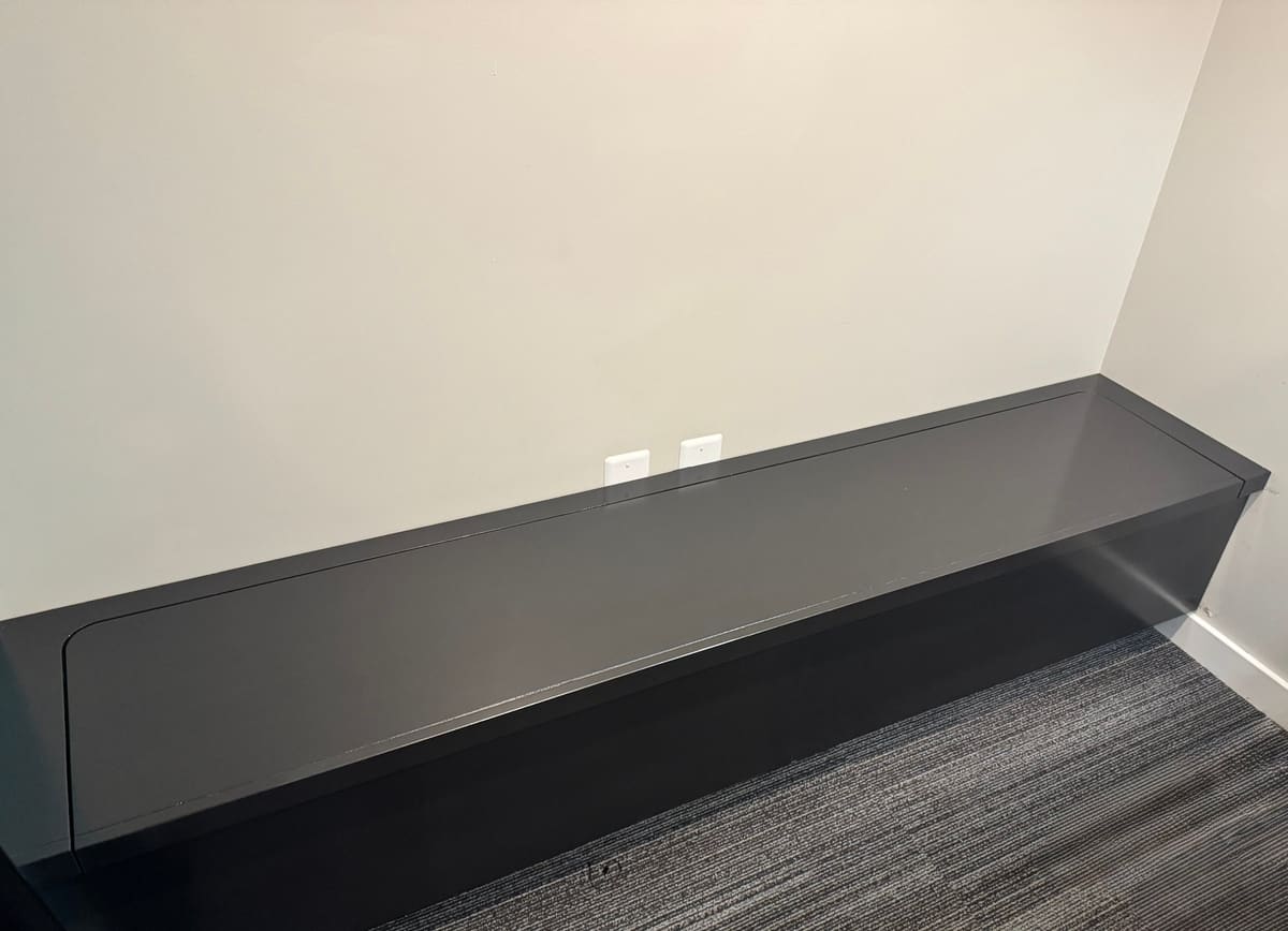 Wall-to-wall built-in bench painted charcoal with a flush lift-up lid in a carpeted room