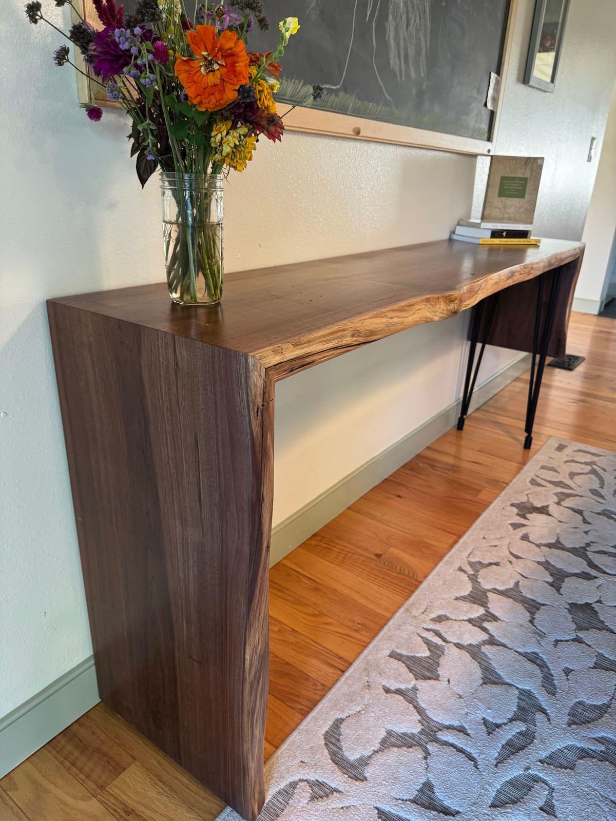 Walnut console with a live edge and a full-height waterfall end, with flowers in a jar on top