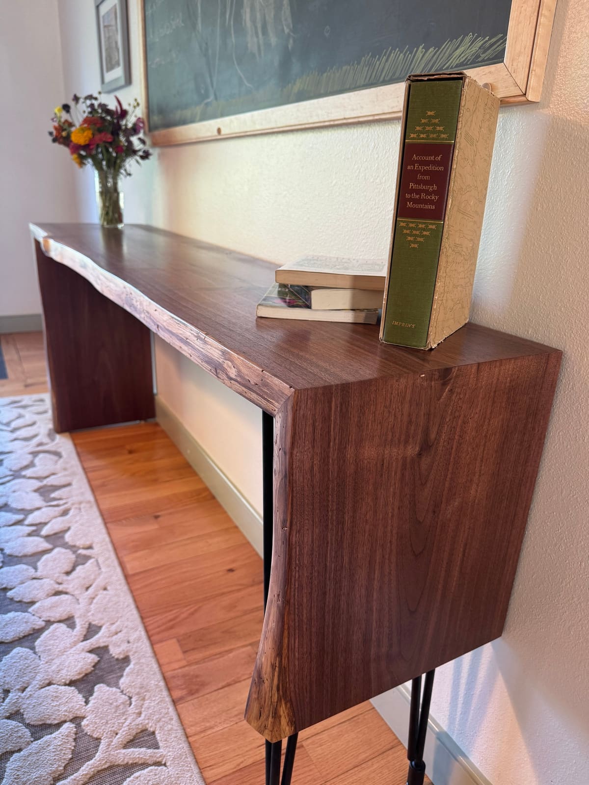 Live-edge walnut console table with a mitered waterfall end and black hairpin legs in a hallway