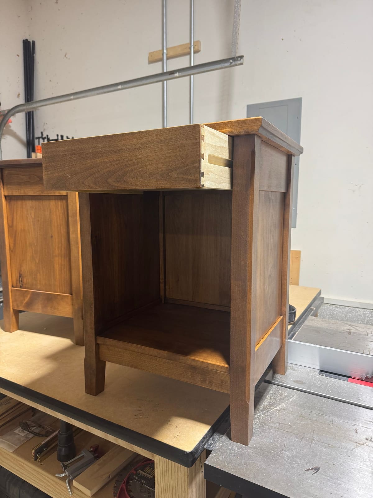 Stained nightstand in the shop with its drawer pulled out to show dovetail joinery