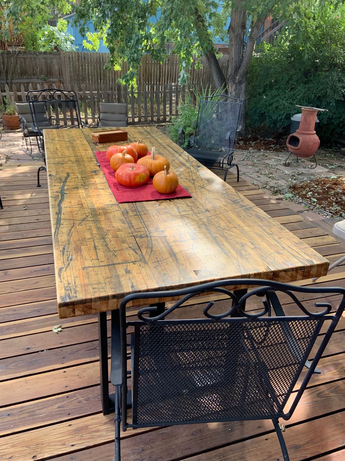 Long outdoor dining table with a thick strip-laminated wood top and black steel base on a backyard deck