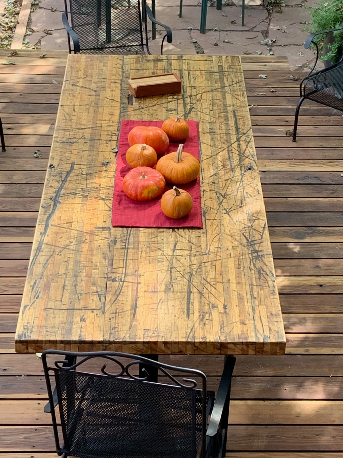 Strip-laminated tabletop with heavy scratches and nail holes, set with pumpkins on a red runner on a deck