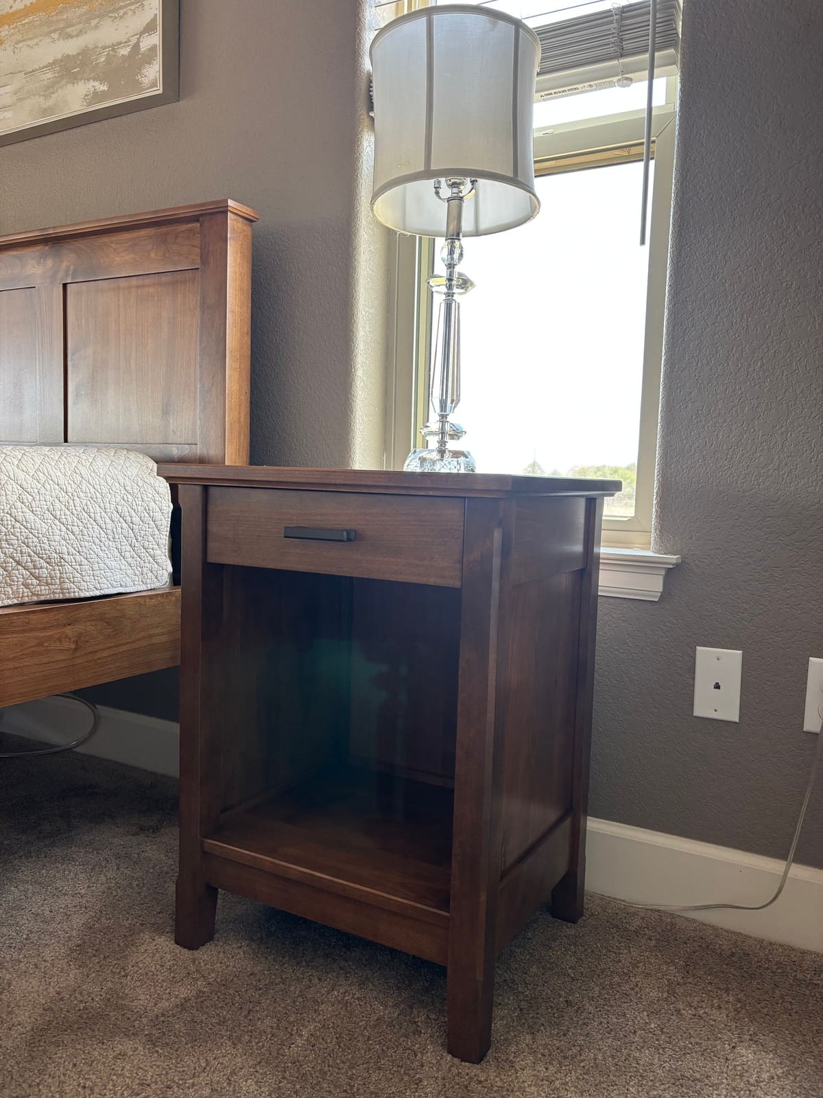 Wood nightstand with one drawer, black bar pull, and open lower shelf beside a matching panel headboard