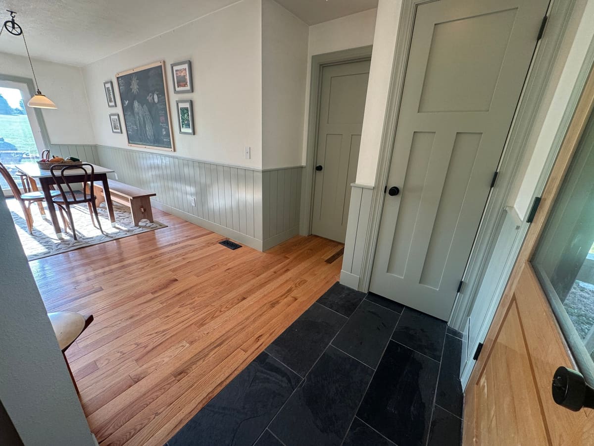 Entry with sage green vertical plank wainscoting and paneled doors opening to a dining area