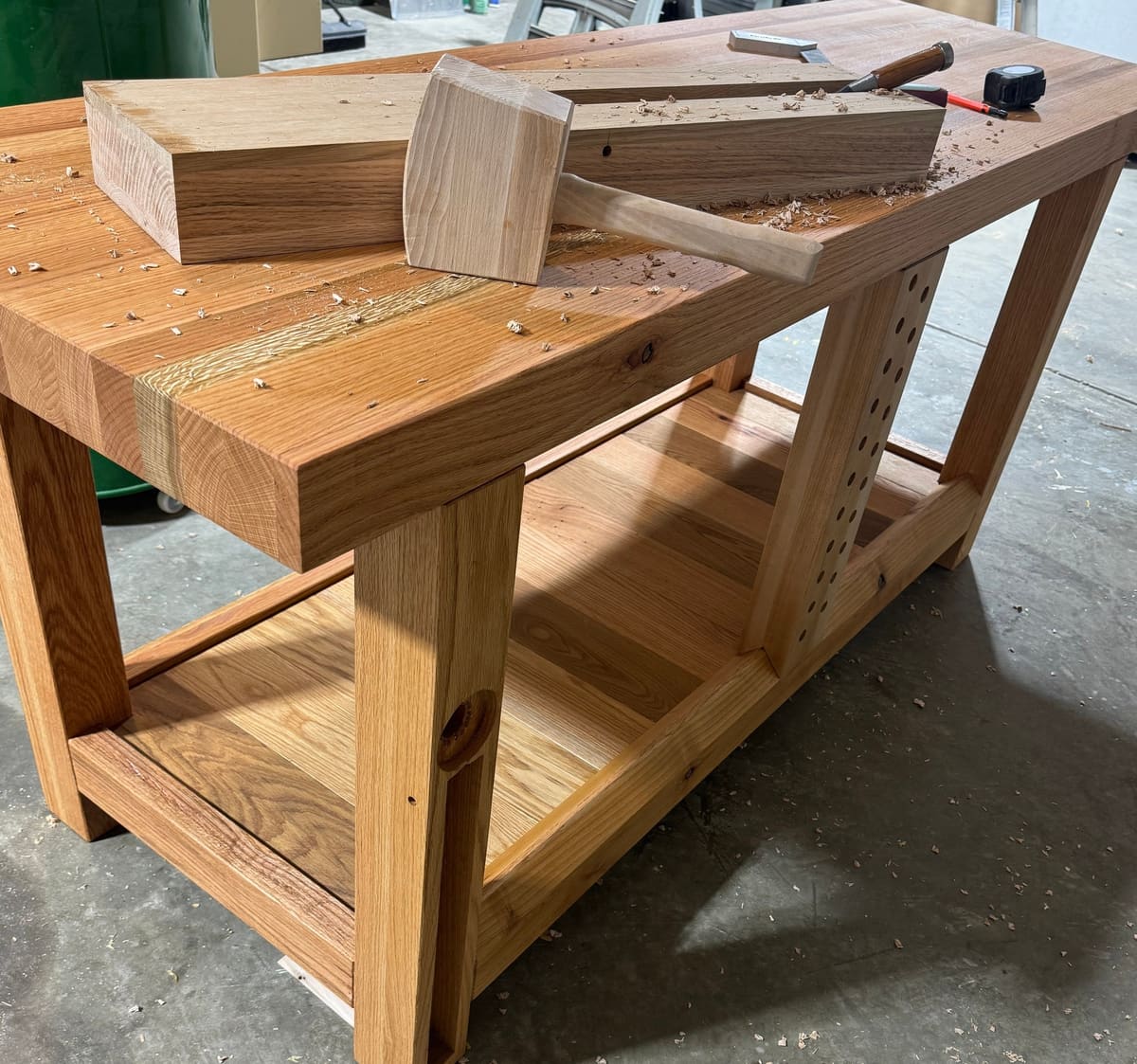 Workbench with a thick laminated top, peg holes in the leg, and a wooden mallet and chisel among shavings