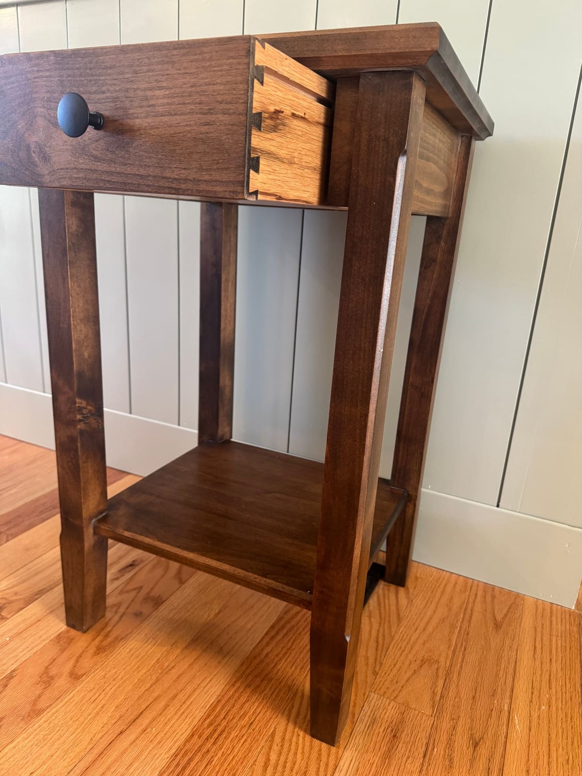 Dark stained nightstand with its drawer pulled open to show dovetail joints, tapered legs and a lower shelf